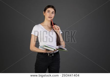 Half Length Portrait Of Thougtful Dreamy Woman Holding Red Pen In Hand Near Mouth, Books In Other Ha