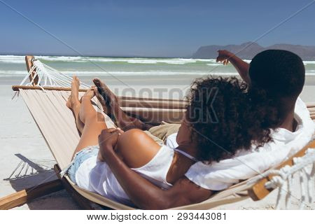 Rear view of cute multi ethnic couple relaxing on hammock while African American male points at something in front of them at beach on sunny day