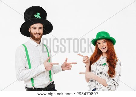 Happy young couple wearing costumes, celebrating St.Patrick 's Day isolated over white background, pointing fingers