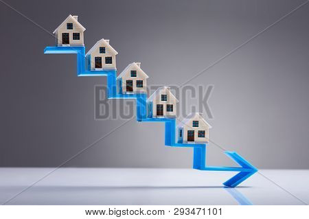 House Models On The Decreasing Staircase Blue Arrow Against Gray Background