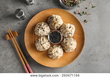Wooden Plate With Tasty Baozi Dumplings And Sesame Seeds Served On Grey Table, Top View