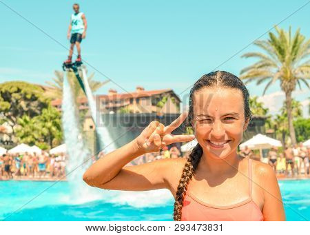 Smiling Teen Girl Enjoing Summer Vacation At The Pool With Fly Board Watershow On The Background. Gi