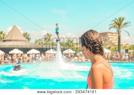 Teen Girl Watching Fly Board Watershow At The Pool. View From The Back. Summer Holidays, Fun Summert