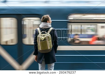 Lonely Adult Handsome Man In A Blue Coat With A Green Backpack Behind Standing On Metro Platform, Tr