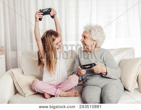 Smiling grandmother with little granddaughter playing games together with gamepads