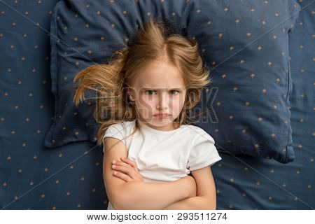 Angry child girl lying on the bed with crossed hands and refuses to sleep