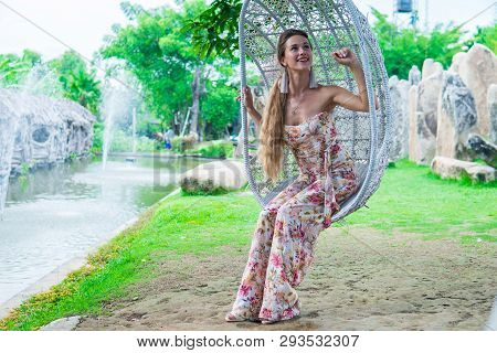 Beautiful Brunette In Dress Swinging On A Swing Over The Water In The Park In Sunny Day