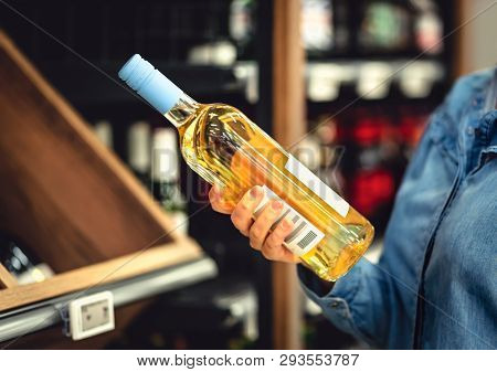 White Wine Bottle In Hand In Liquor Store. Customer Buying Alcohol. Woman Choosing The Right Bottle 