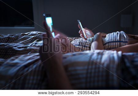 Bored Distant Couple Ignoring Each Other Lying In Bed At Night While Using Mobile Phones. Smartphone