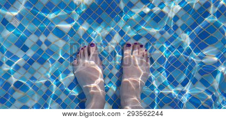 Two Female Bare Feet Seen Through Blue Waters Of A Swimming Pool