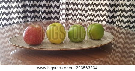 A Dish With Four Apples Of Various Colors Stay On Glass Table