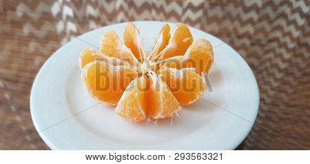 A White Plate With Peeled Mandarin Slices Stand On Glass Table With Black And White Pattern Reflecti