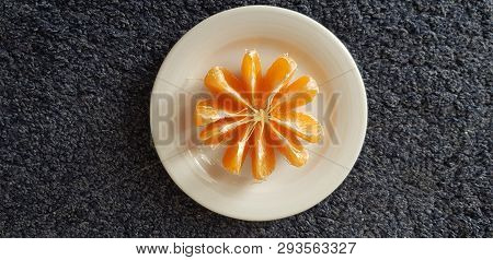 A White Plate With Peeled Mandarin Slices Stand On Dark Surface
