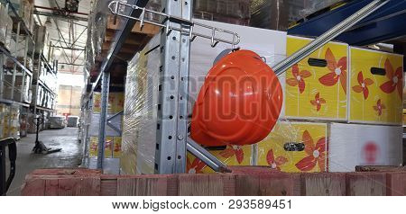 Orange Worker Safety Helmet Hang On The Hook Inside Warehouse Full Of Boxes