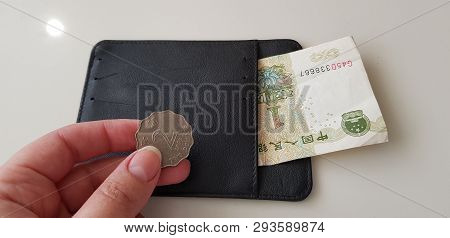 Female Hand Holds Two Hong Kong Dollars Coin Over Black Wallet With One Yuan Banknote In It