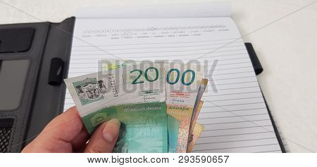 Serbian Dynars Banknotes In Female Hand Over Open Notebook With Marked April Dates In Calendar