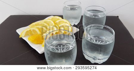 Four Glasses With Vodka On Brown Table Around White Plate With Lemon Slices
