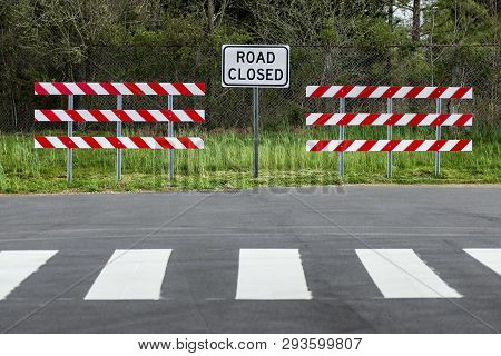 Horizontal Shot Of Two Red And White Striped Barriers With A Road Closed Sign In The Middle Of Them.