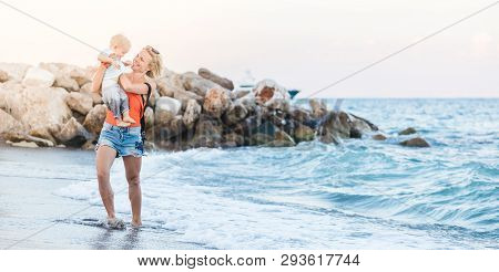 Woman Playing With Her Baby Outside Against The Sea. The Concept Of A Happy Full-fledged Family Life