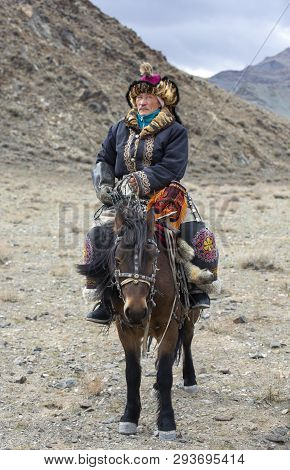 Kazakh Eagle Hunter Traveling On His Horse In A Landscape Of Altai Mountains