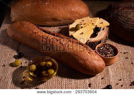 Fresh Bread Baguette With Olive Oil, Olives. Cheese And Rosemary On Wooden Background. Teasty Breakf