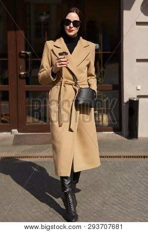 Portrait Of Young Tall Beautiful Woman On Urban Background. Stylish Lady Buys Coffee And Walks Along