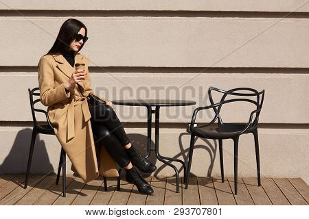 Brunette Beautiful Young Lady Sits On Terrace, Drinks Aromatic Hot Coffee, Having Beige And Black Lo