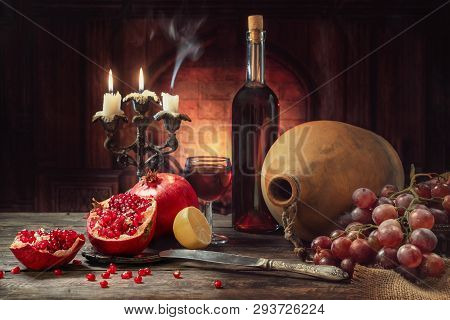 Still Life In A Rustic Style. Fruit-pomegranates, Grapes And Lemon Lying On A Wooden Table With A Bo