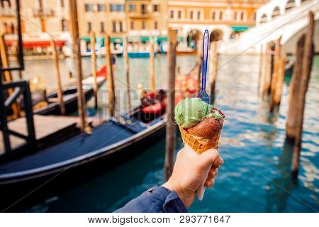 Man Hand Holds The Horn Of Real Italian Pistachio Ice Cream Fork Inside, In Background Blurred House