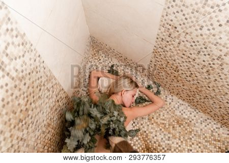 Slim Woman In Bath Is Getting Steaming Massage With Hot Oak Leaves Brooms, In Steam-room