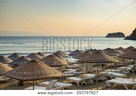 Beach Umbrellas And Chaise Lounges With Sea And Evening Sky In The Background.
