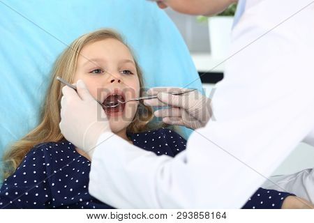 Little Baby Girl Sitting At Dental Chair With Open Mouth And Feeling Fear During Oral Check Up While