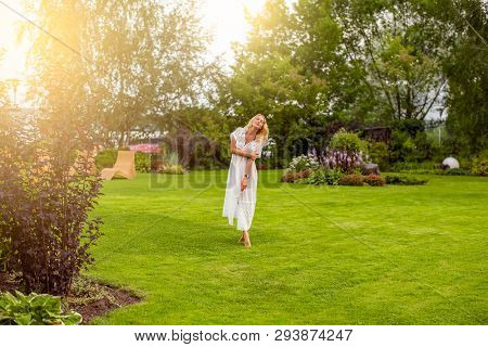 Youmg Beautiful Blond Woman In Beautiful Summer Garden Is Barefoot On Lawn