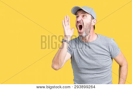 Handsome middle age hoary senior man wearing sport cap over isolated background shouting and screaming loud to side with hand on mouth. Communication concept.
