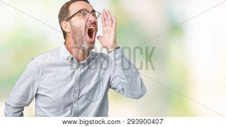 Handsome middle age elegant senior man wearing glasses over isolated background shouting and screaming loud to side with hand on mouth. Communication concept.