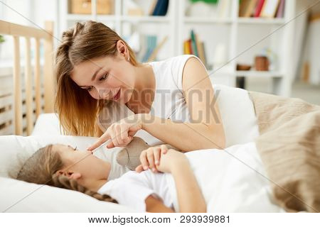 Portrait Of Loving Young Mother Laying In Bed With Daughter And Touching Her Nose Playfully, Copy Sp