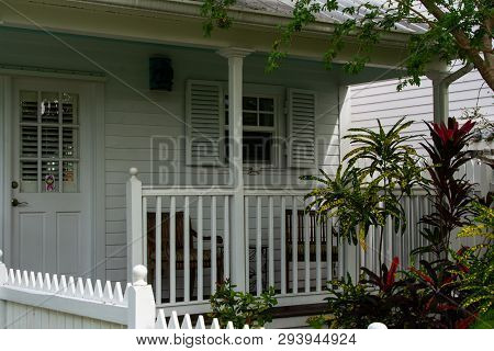 Front Porch On A White House Framed By Tropical Plants Giving A Peek Into A Relaxing Lifestyle