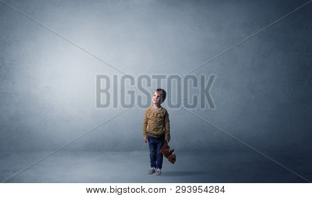Little waggish kid staying alone in a big empty room with his plush