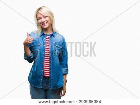 Young beautiful blonde woman wearing denim jacket over isolated background doing happy thumbs up gesture with hand. Approving expression looking at the camera with showing success.