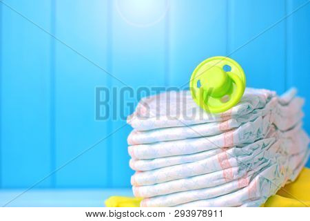 Baby Accessories Background. Pile Of Diapers With Dummy.
