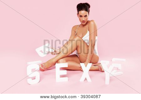 Belle femme sexy en maillot de bain posant assis sur le sol avec le mot SEXY en blanc l capital