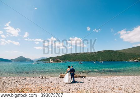 Bride And Groom Are Hugging On The Beach Of The Mamula Island Against The Backdrop Of The Ancient Fo