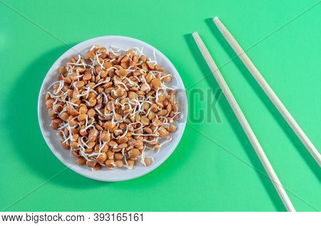 Plate With Lentil Sprouts And Chopsticks On A Green Table