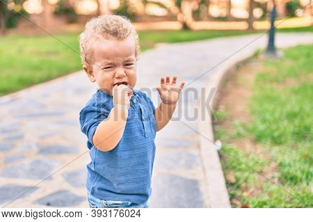 Cute and sad little boy crying having a tantrum at the park on a sunny day. Beautiful blonde hair male toddler frustrated with tears on face outdoors