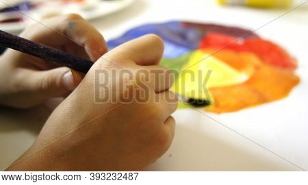Close-up Of Baby Hand Drawing With Paintbrush Of Gouache Paints On Sheet Of Paper Color Circle. Chil