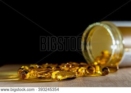 Close-up Of Yellow Pills Of Gold Fish Oil For Good Health On Wooden Table And Black Background. Food