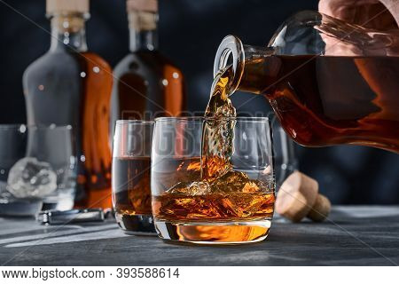 Two Glasses Of Whiskey With Ice On A Concrete Table, A Glass Of Whiskey Is Poured From A Bottle. Two