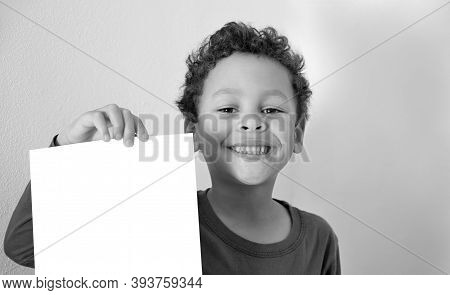 Little Boy Showing Blank White Piece Of Paper With Grey Background Stock Photo