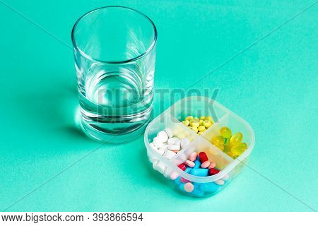A Glass Of Water And Medical Pills In A Box. Pillbox With Multi-colored Pills