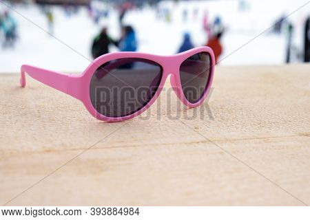 Pink-rimmed Sunglasses On Wooden Slope In Apres Ski Bar Or Cafe, With Ski Slope In Background, Copy 